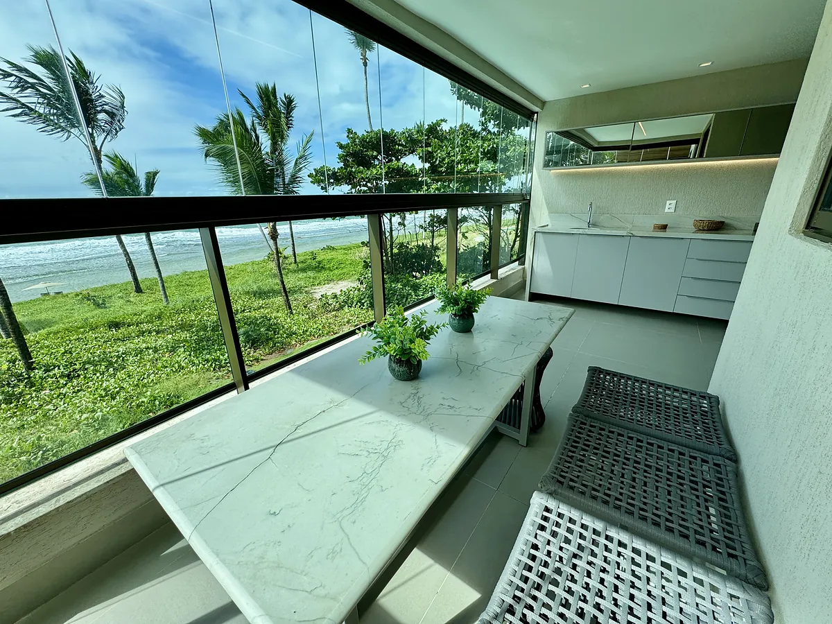Varanda gourmet de uma unidade, com bancada em mármore e o mar visível através do fechamento em vidro.