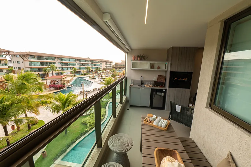 Varanda gourmet de apartamento do Polinésia Villa, com churrasqueira, bancada e vista para as piscinas do resort.
