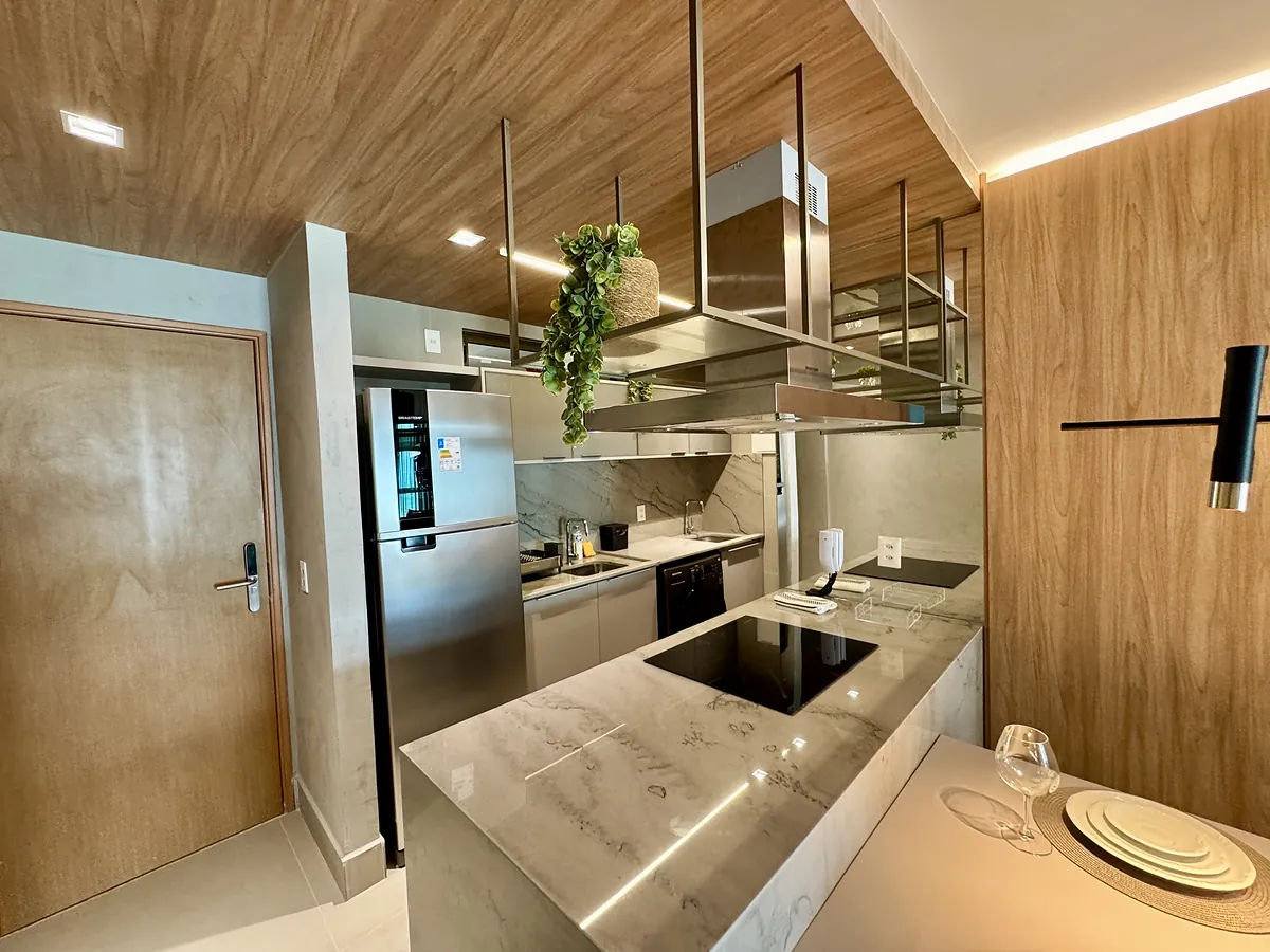 Cozinha completa e integrada com bancada e frontão em mármore, marcenaria em madeira e coifa central.