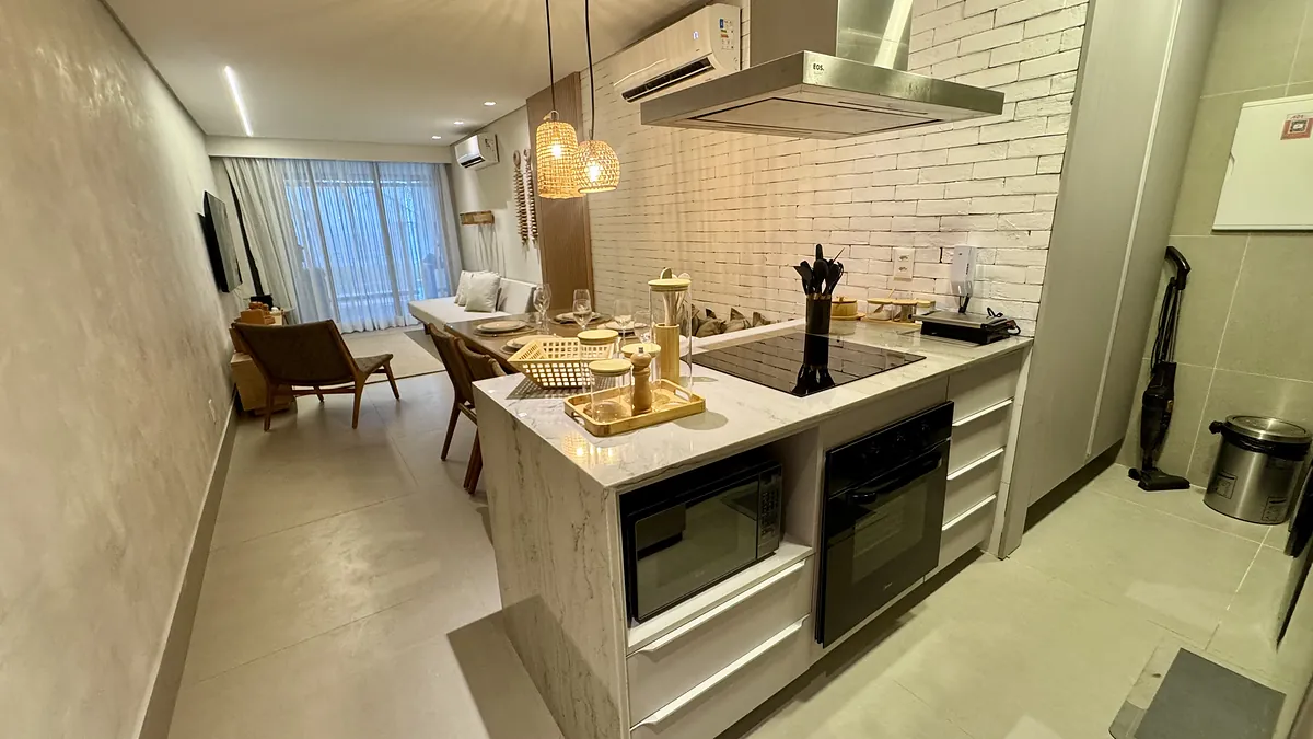 Cozinha com ilha em mármore, forno e cooktop embutidos, aberta para a sala.