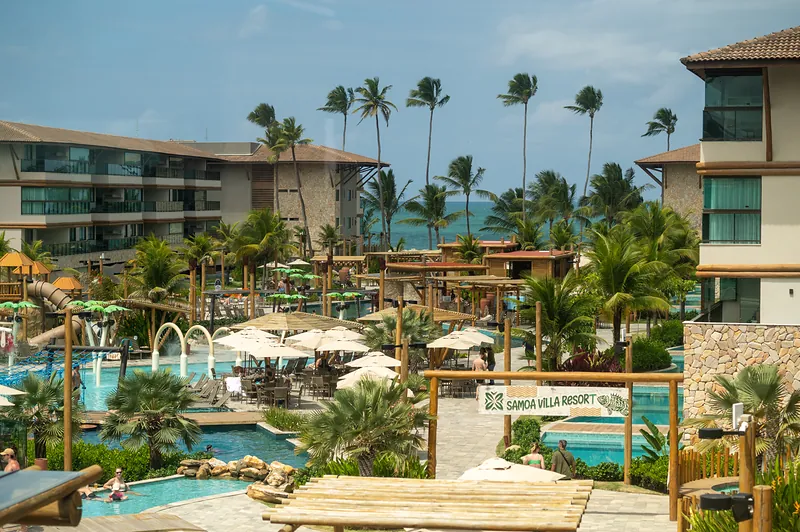Vista panorâmica do Samoa Villa Resort, com piscinas, coqueiros e o mar ao fundo.