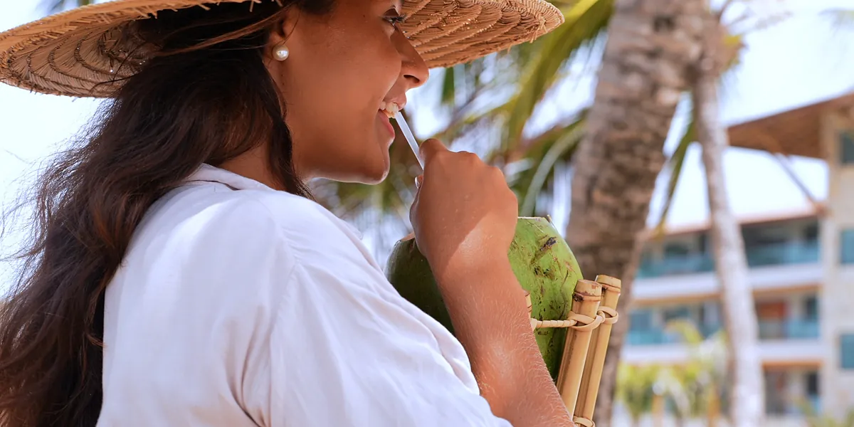 Hóspede com água de coco à sombra dos coqueiros.